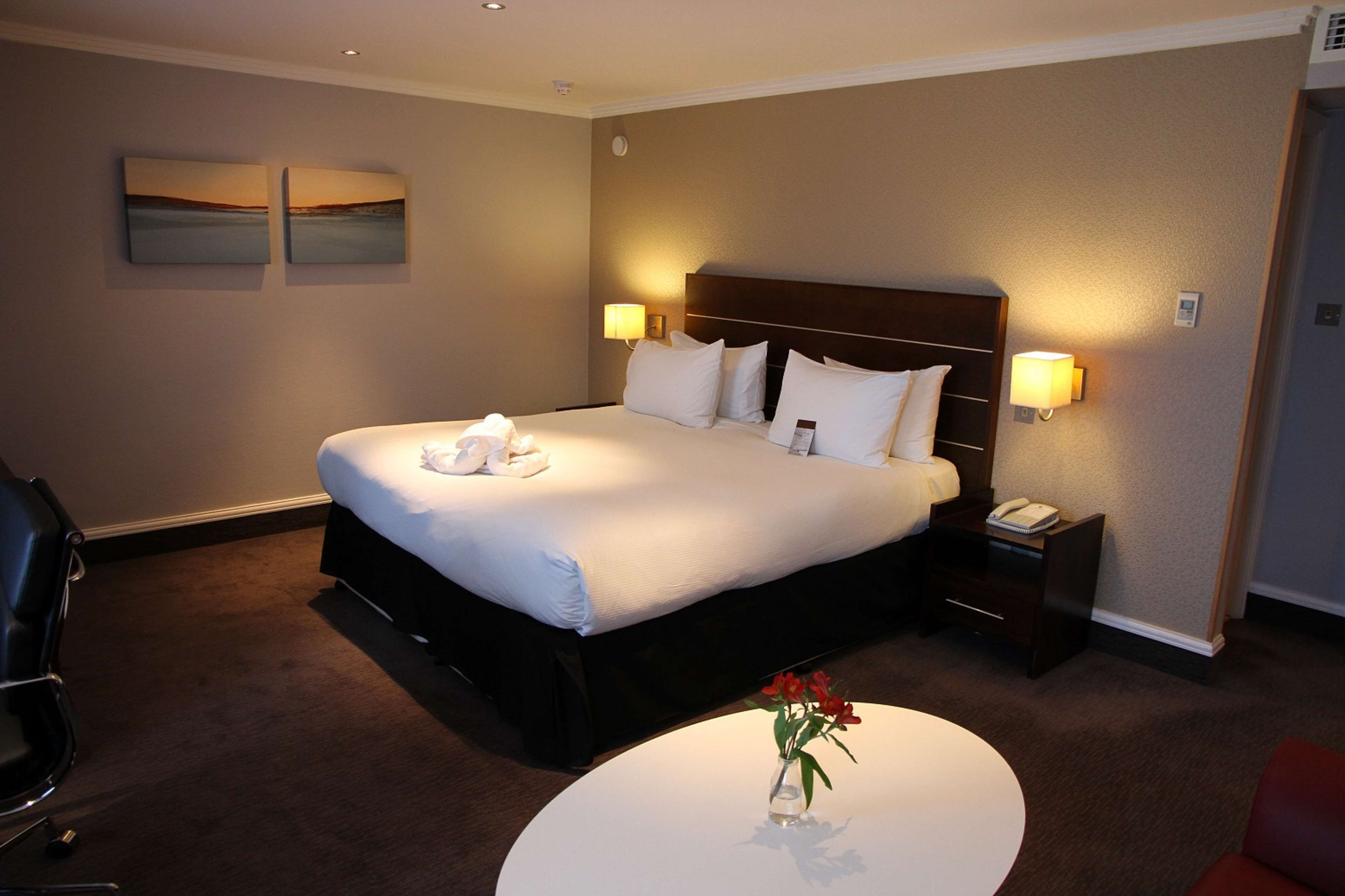 Habitación de hotel con una cama grande, lámparas de noche, mesita de noche, escritorio y una silla.