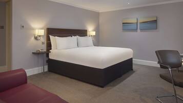 A hotel room with a large bed, two bedside lamps, a desk with a chair, and two landscape paintings on the wall.