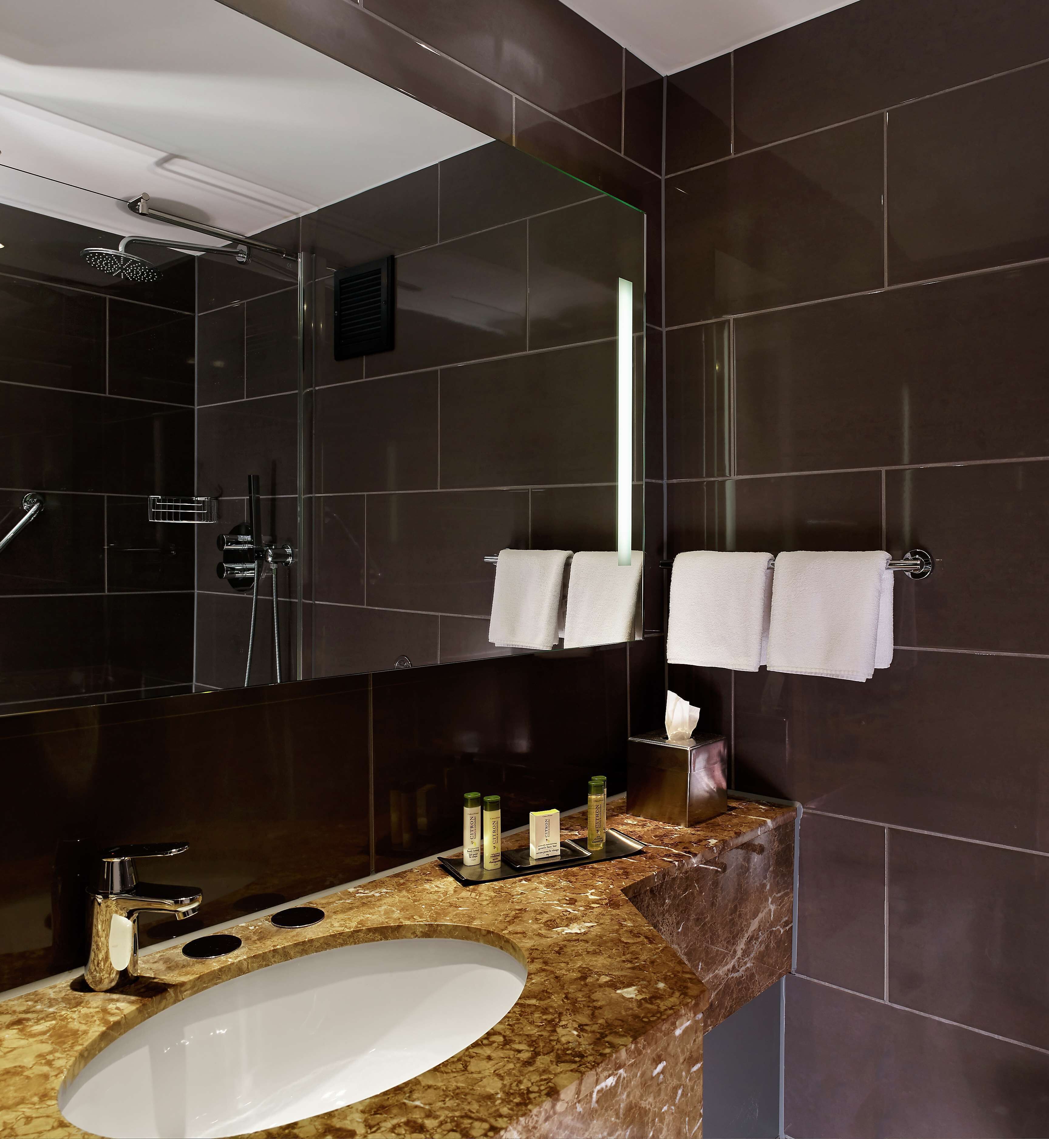 A modern bathroom with a large mirror, dark tiles, a marble countertop, a sink, and a shower area.