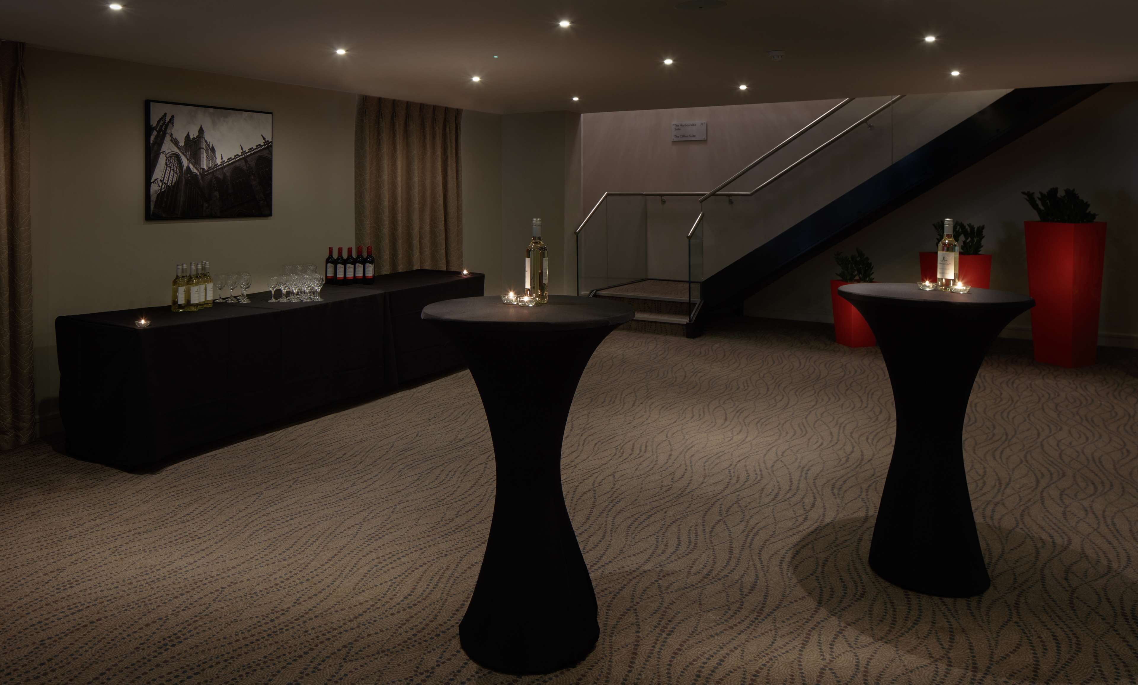 A hotel lobby with a reception desk, a staircase, and two tables with candles.