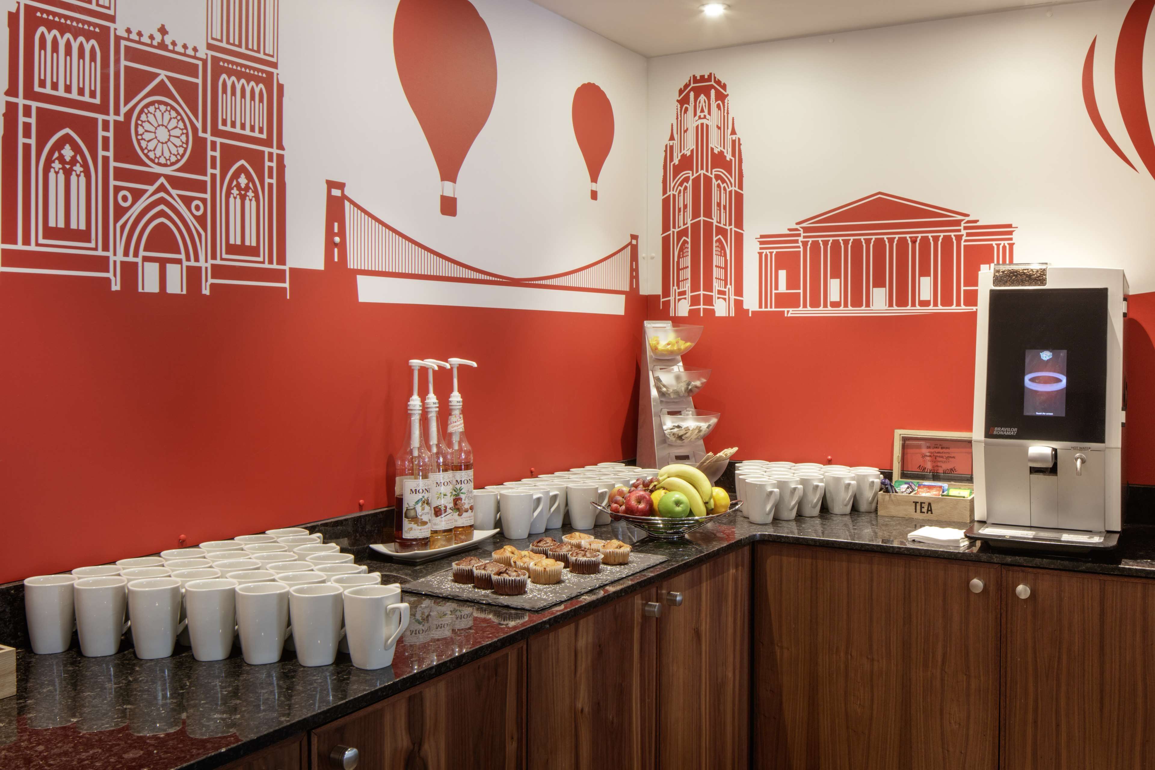 Balcão de café da manhã com máquina de café, uma cesta de frutas e uma bandeja de muffins.