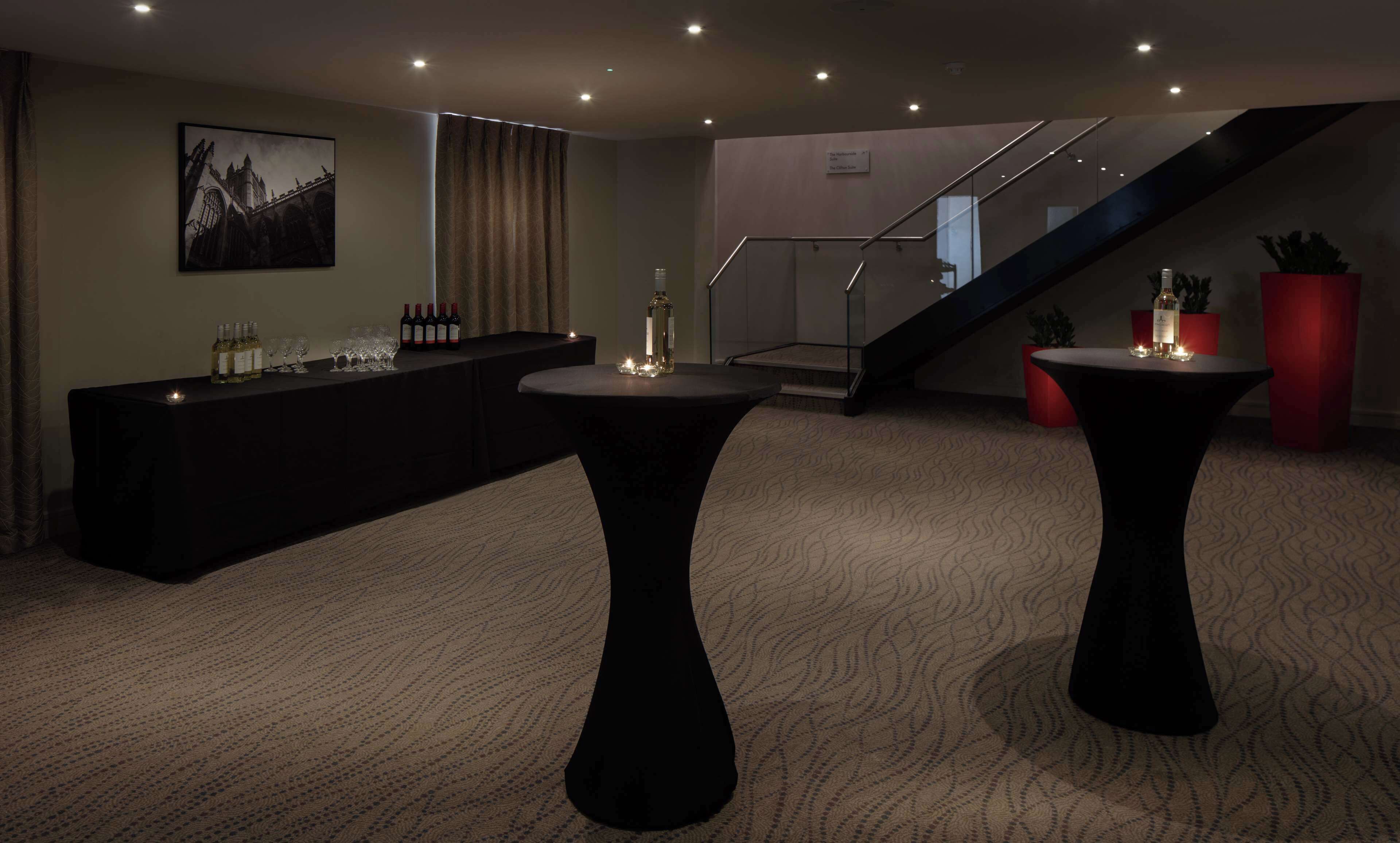 A modern hotel lobby with a bar area, a staircase, and two round tables with candles.