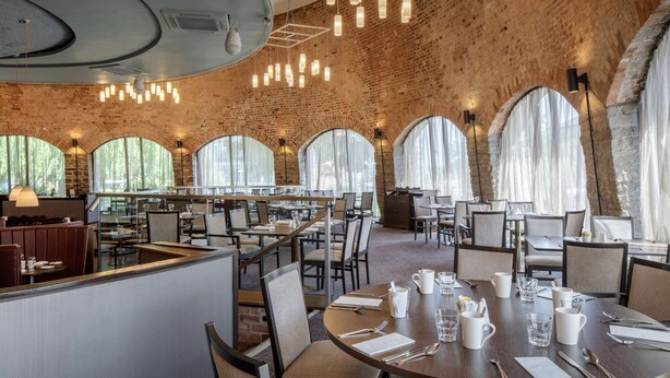 A spacious restaurant with high ceilings, exposed brick walls, and large arched windows allowing natural light. Tables are neatly arranged with chairs, and the space is well-lit with pendant lighting. - Doubletree by Hilton Bristol (Bristol)
