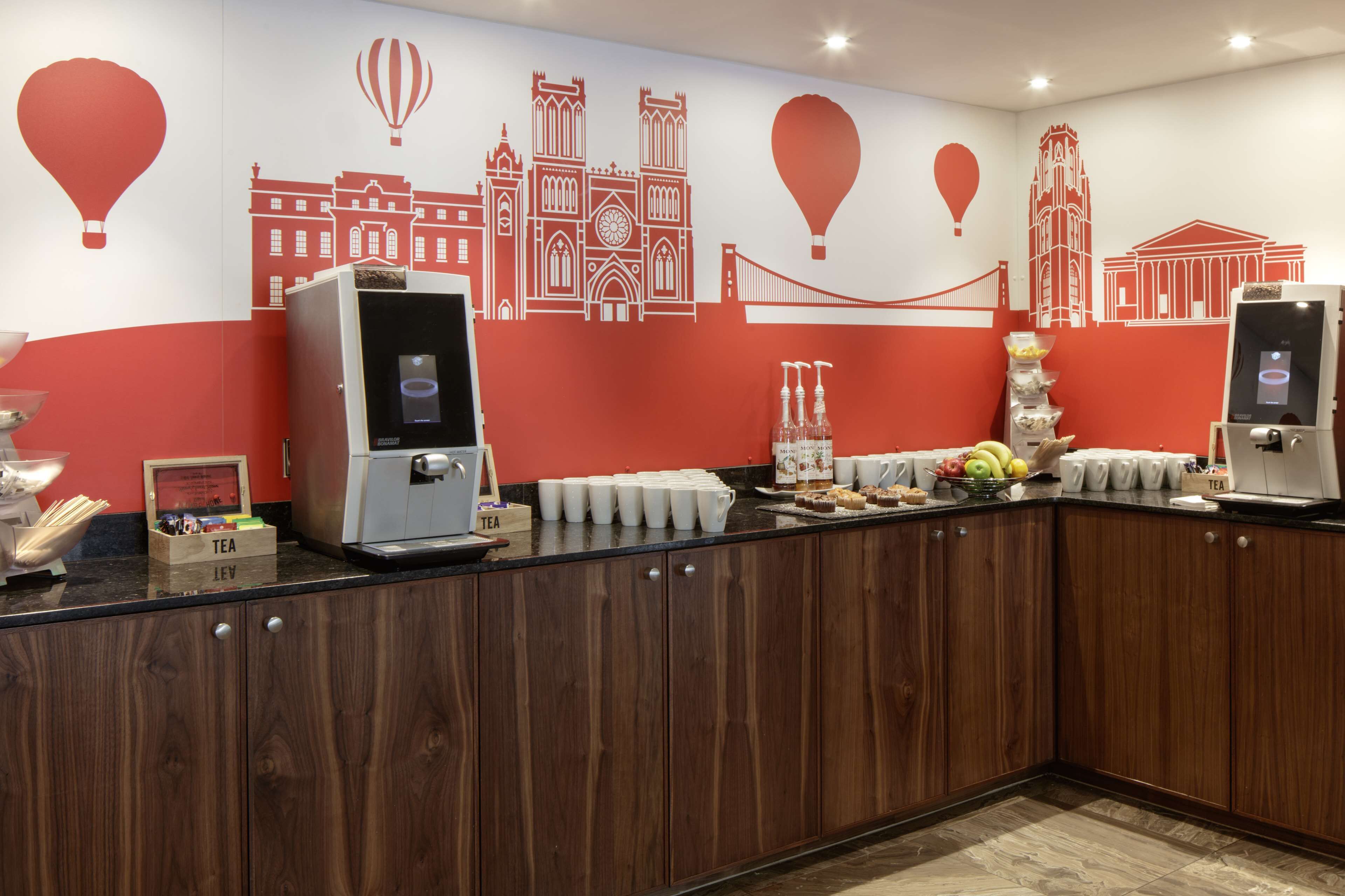 Een ontbijtbuffet met koffieapparaten, thee en een schaal fruit.