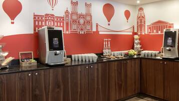 Een ontbijtbuffet met koffieapparaten, thee en een schaal fruit.
