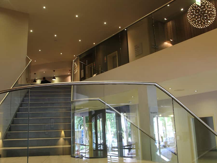 Un interior moderno con una escalera de barandilla de vidrio, un accesorio de iluminación circular y un área de recepción.