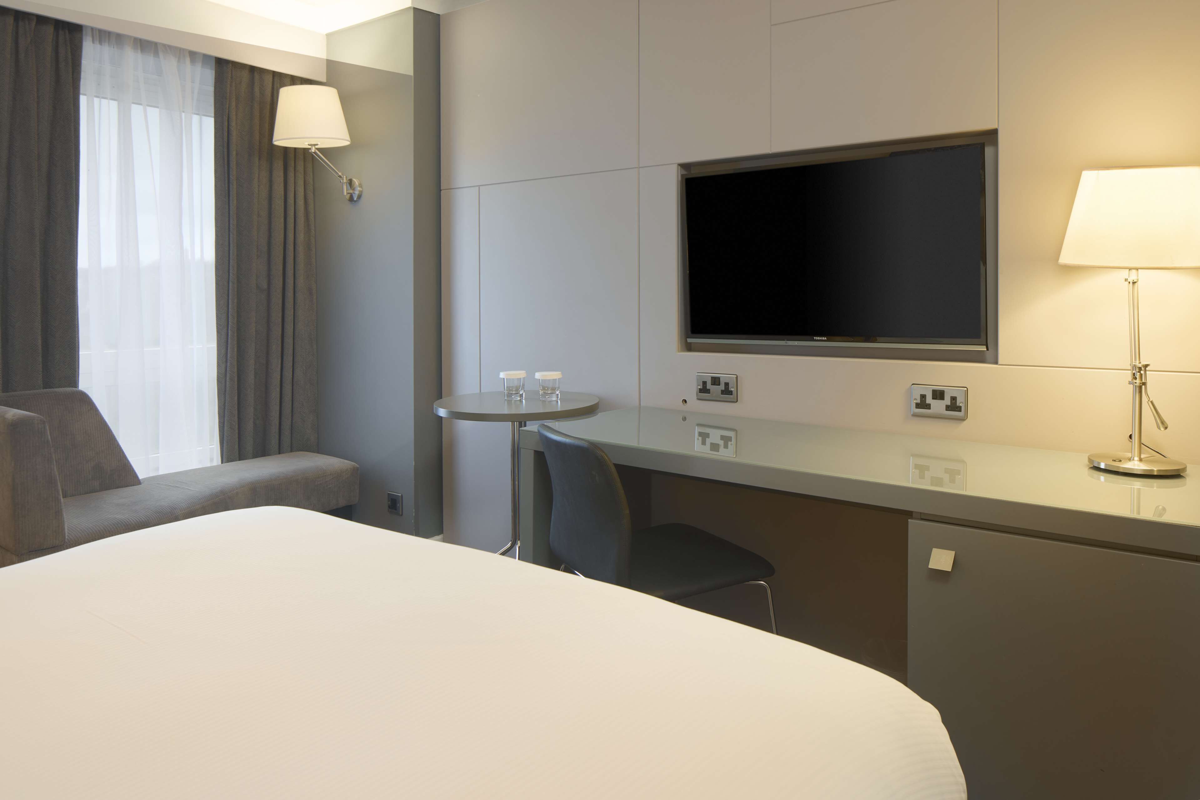 Una habitación de hotel con una cama, un escritorio, una silla, un televisor y una lámpara.