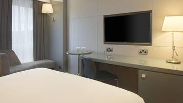Una habitación de hotel con una cama, un escritorio, una silla, un televisor y una lámpara.