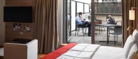 A hotel room with a bed, a TV, a desk, and a balcony with seating.