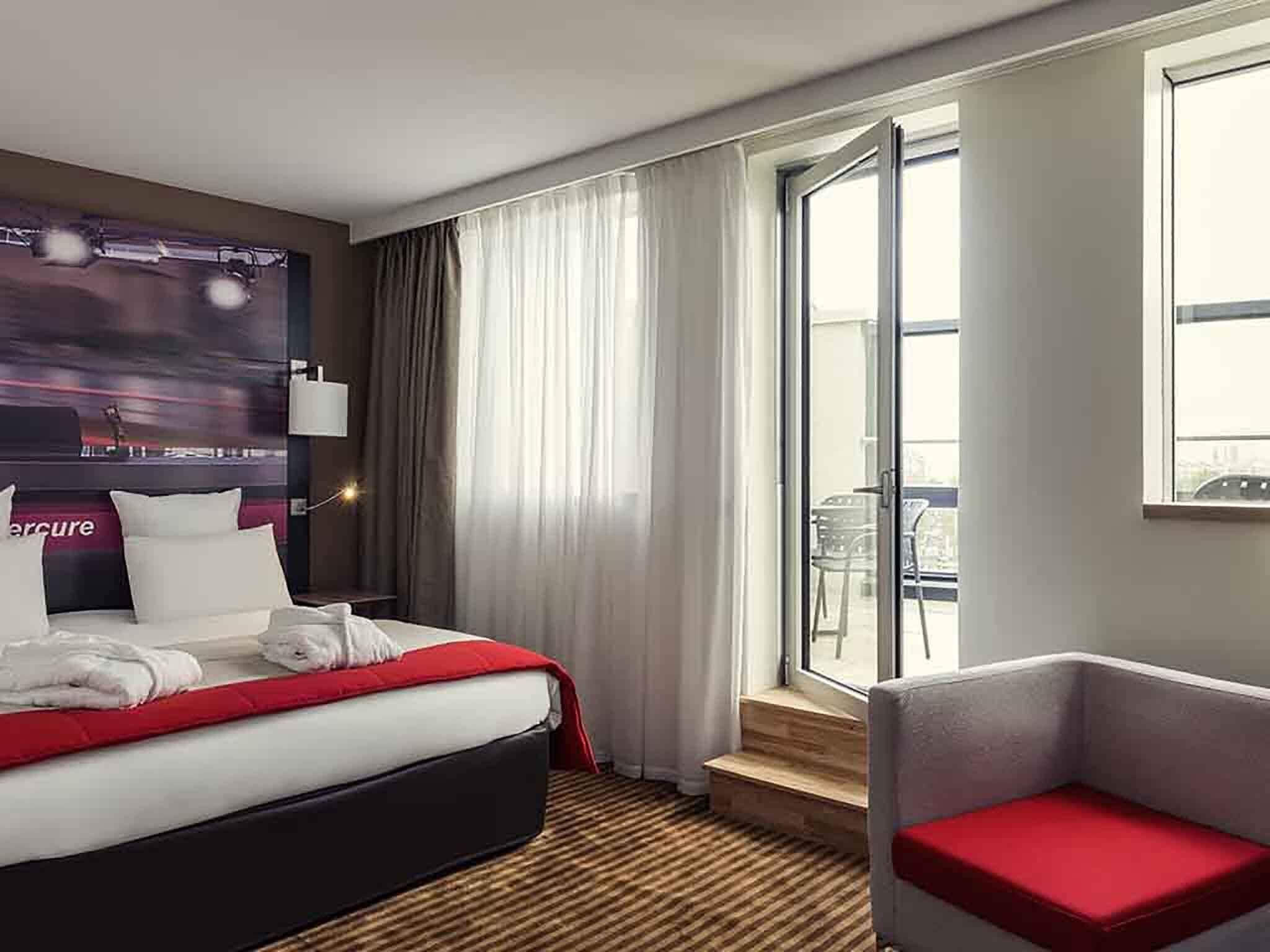 A hotel room with a bed, a chair, a window, and a view of the outside.