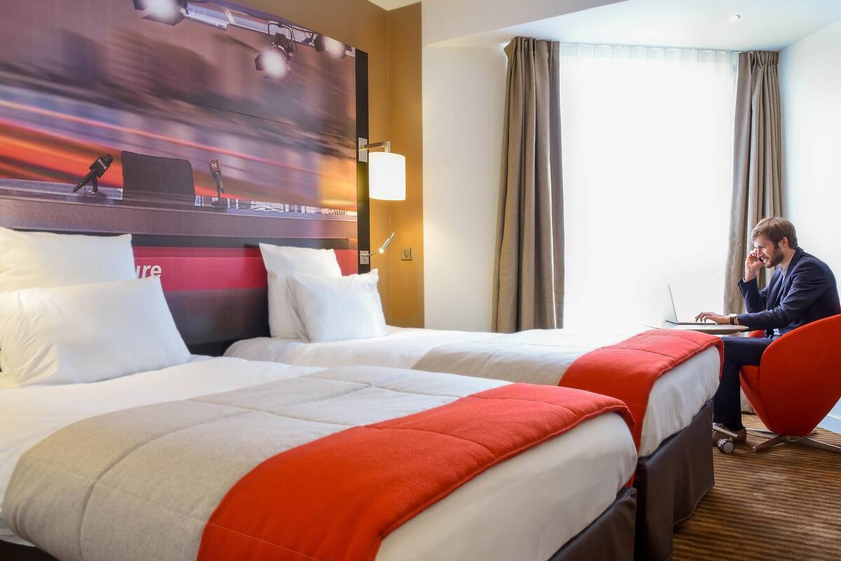 A hotel room with two beds, a desk, a chair, and a large abstract painting on the wall.