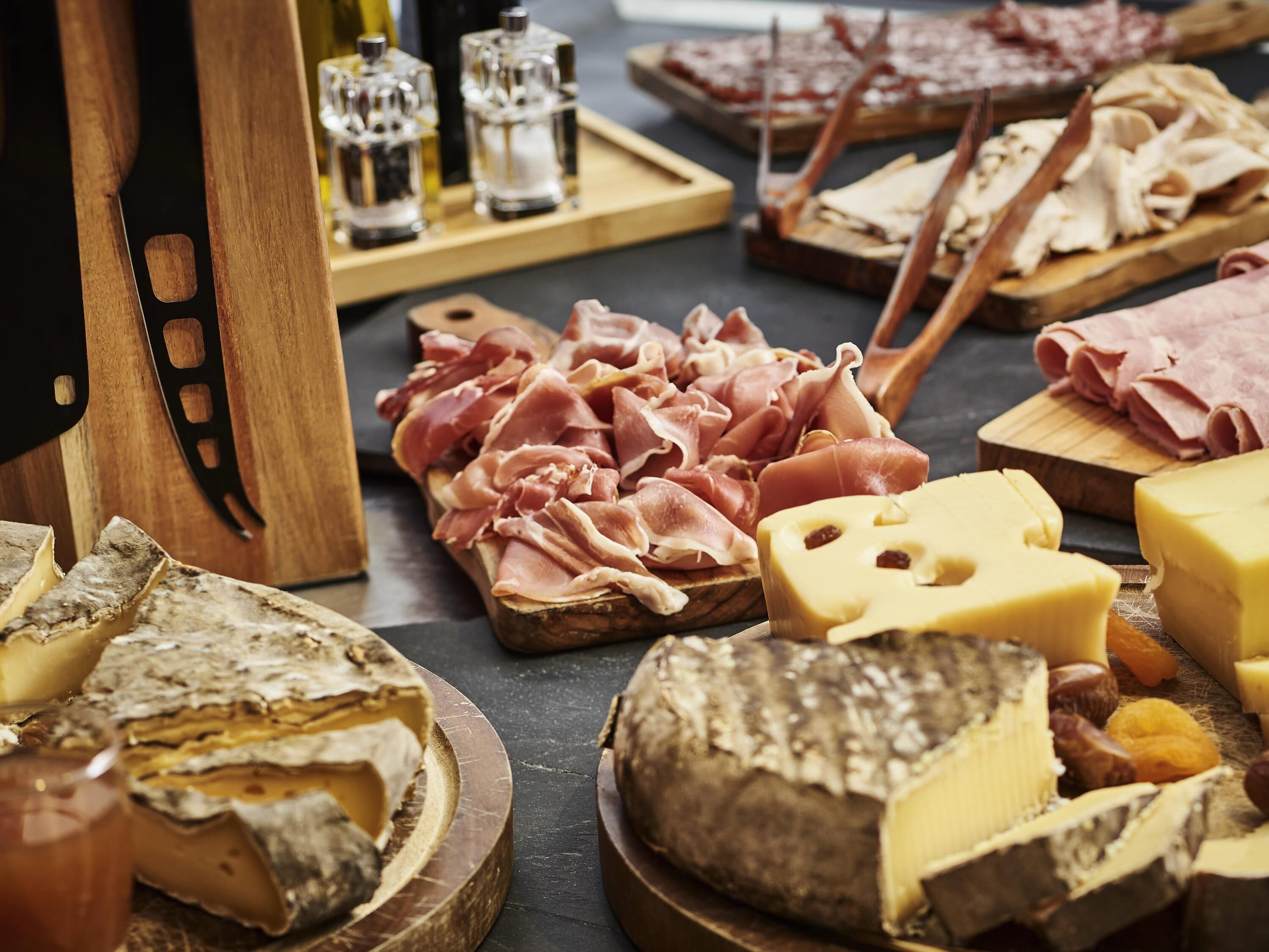 A variety of cheeses, cured meats, and a wooden cutting board on a table.