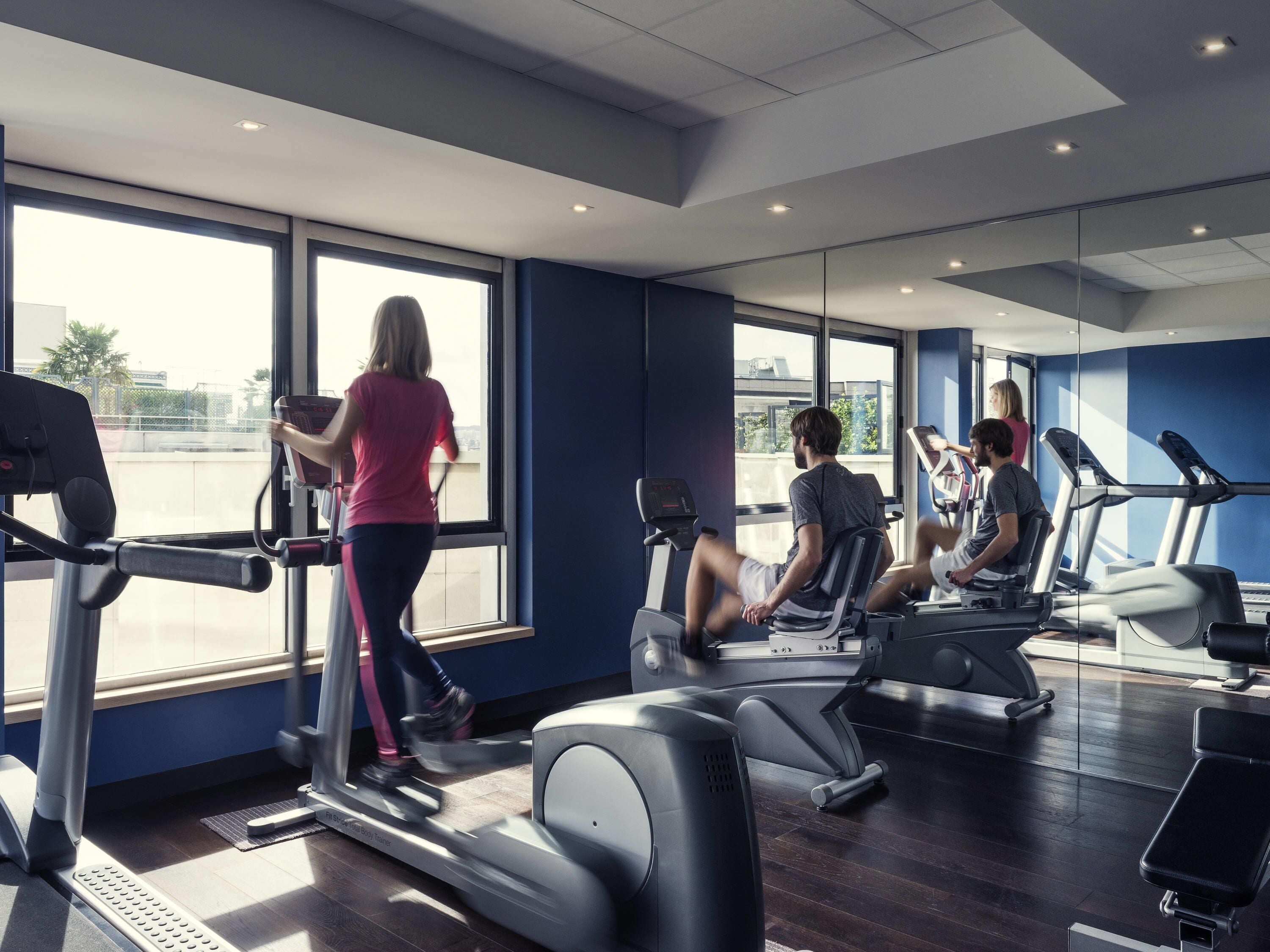 Uma academia com esteiras, bicicleta ergométrica e um painel de espelhos.