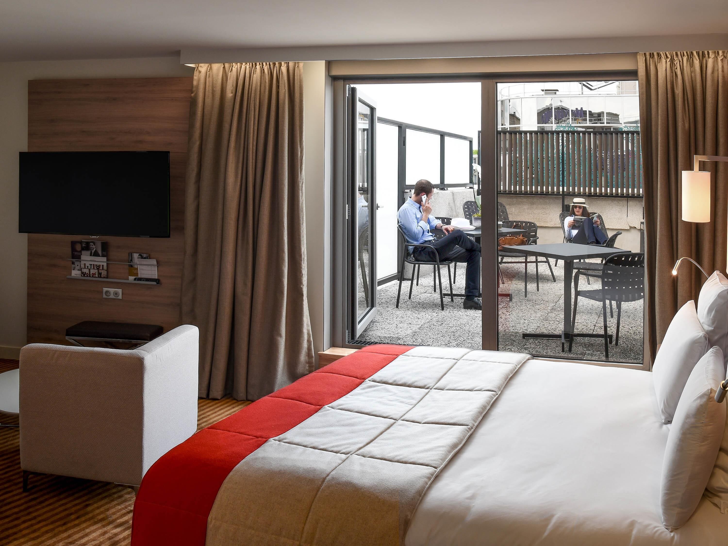 Une chambre d’hôtel équipée d’un lit, d’une télévision, d’un bureau et d’un balcon avec une table et des chaises.