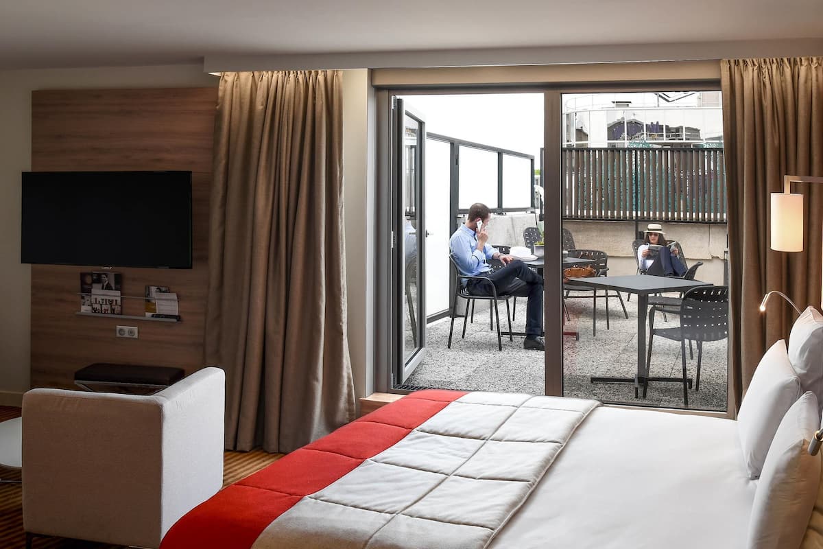 Une chambre d’hôtel équipée d’un lit, d’une télévision, d’un bureau et d’un balcon avec une table et des chaises.