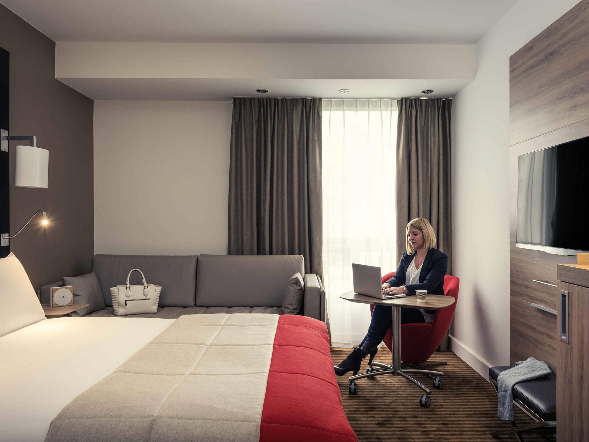 Quarto de hotel moderno com uma cama, uma escrivaninha, um laptop e uma televisão.