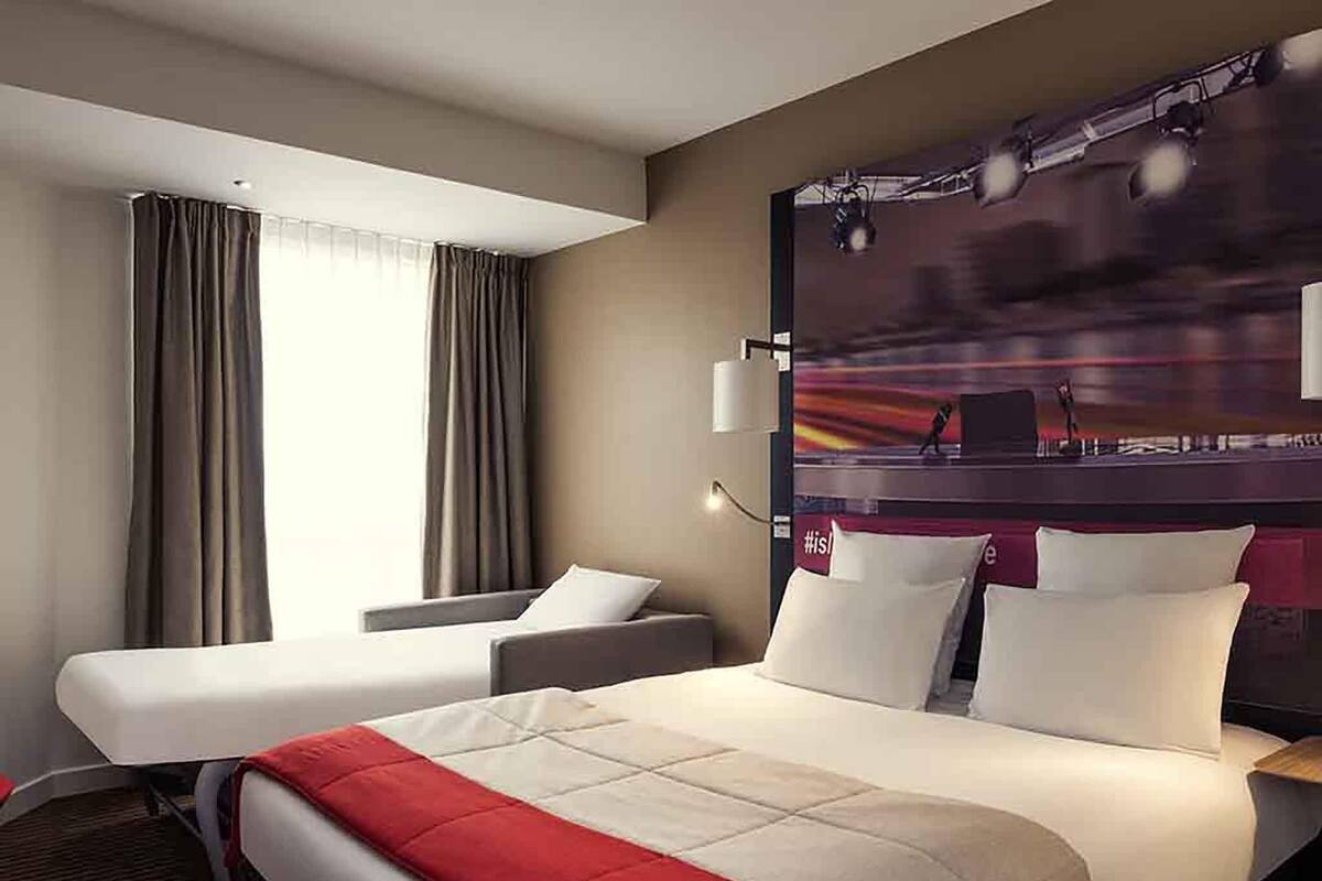 A hotel room with a bed, a desk, a chair, and a large window with curtains.