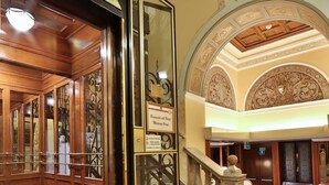 Un vaste hall d’entrée avec un tapis rouge, un escalier agrémenté d’une balustrade et des décorations ornementales au plafond.