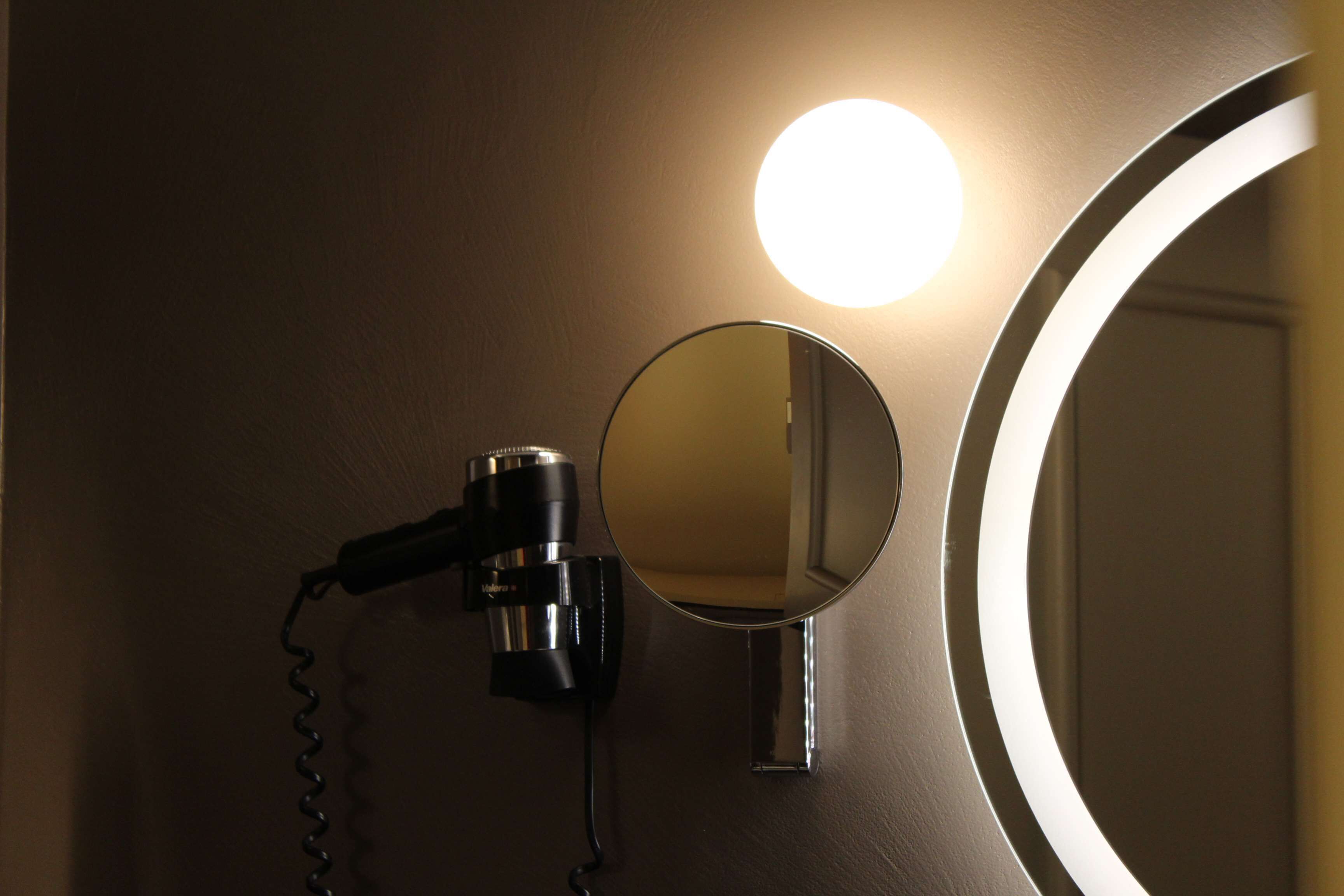 A hairdryer mounted on a wall with a mirror and a round light fixture.