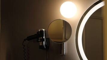 A hairdryer mounted on a wall with a mirror and a round light fixture.