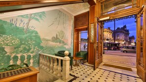 Un hall d’hôtel orné d’une fresque murale, avec un escalier et une vue sur la rue.