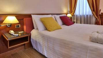 Et hotelværelse med en pænt redt seng, et sengebord med lampe, telefon og en lille hylde.