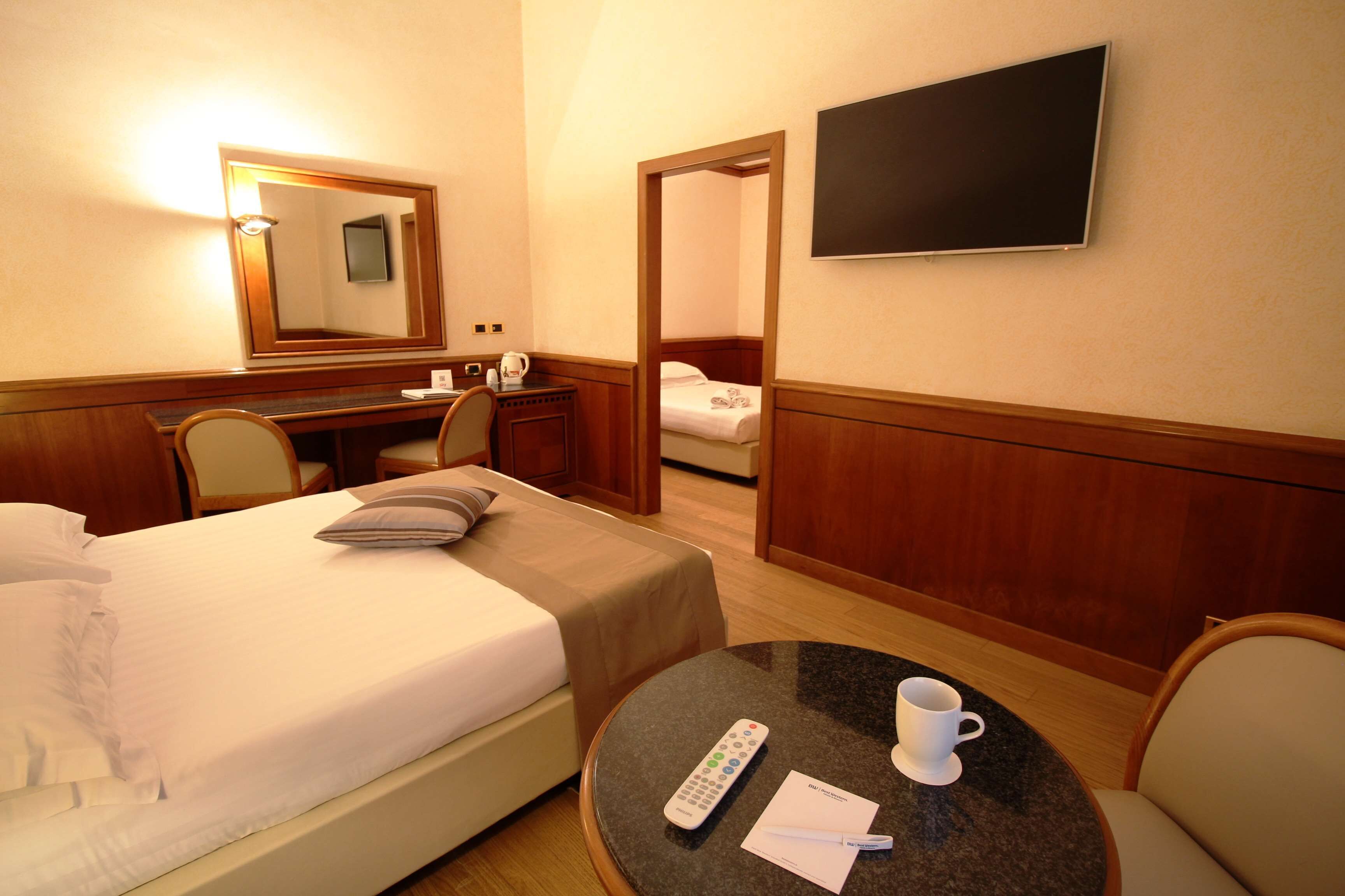 Une chambre d’hôtel comprenant un lit, un bureau, une chaise, une petite table ronde avec une télécommande et une tasse, ainsi qu’un téléviseur fixé au mur.