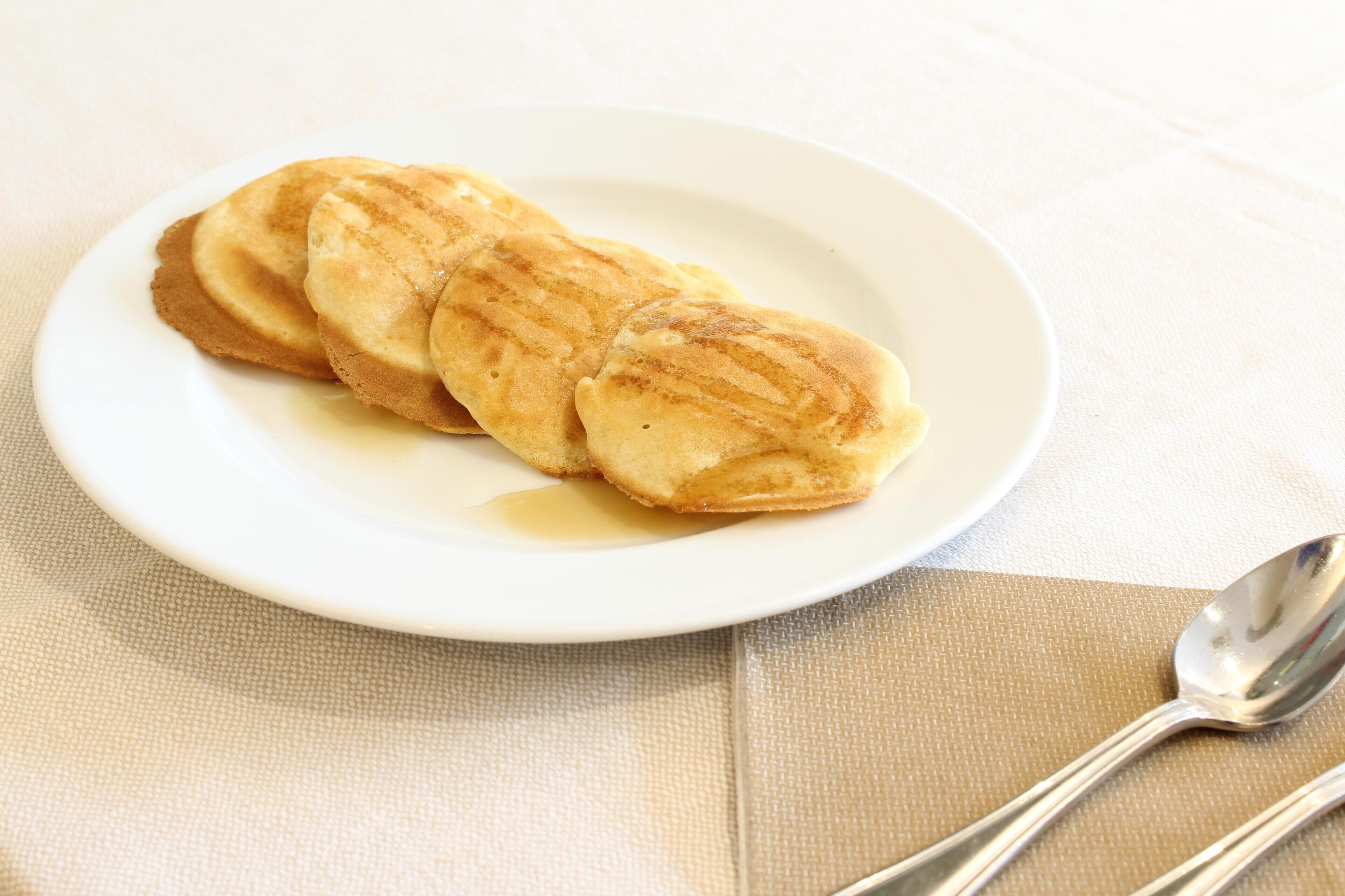 Een stapel pannenkoeken met stroop op een wit bord, met een lepel erbij.