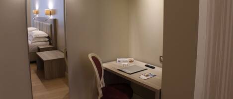 Een hotelkamer met een bed, nachtkastje, stoel, bureau en een spiegel die de kamer weerspiegelt.