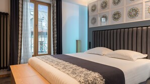 Habitación de hotel con una cama grande, un banco, vistas al exterior y decoración en la pared.