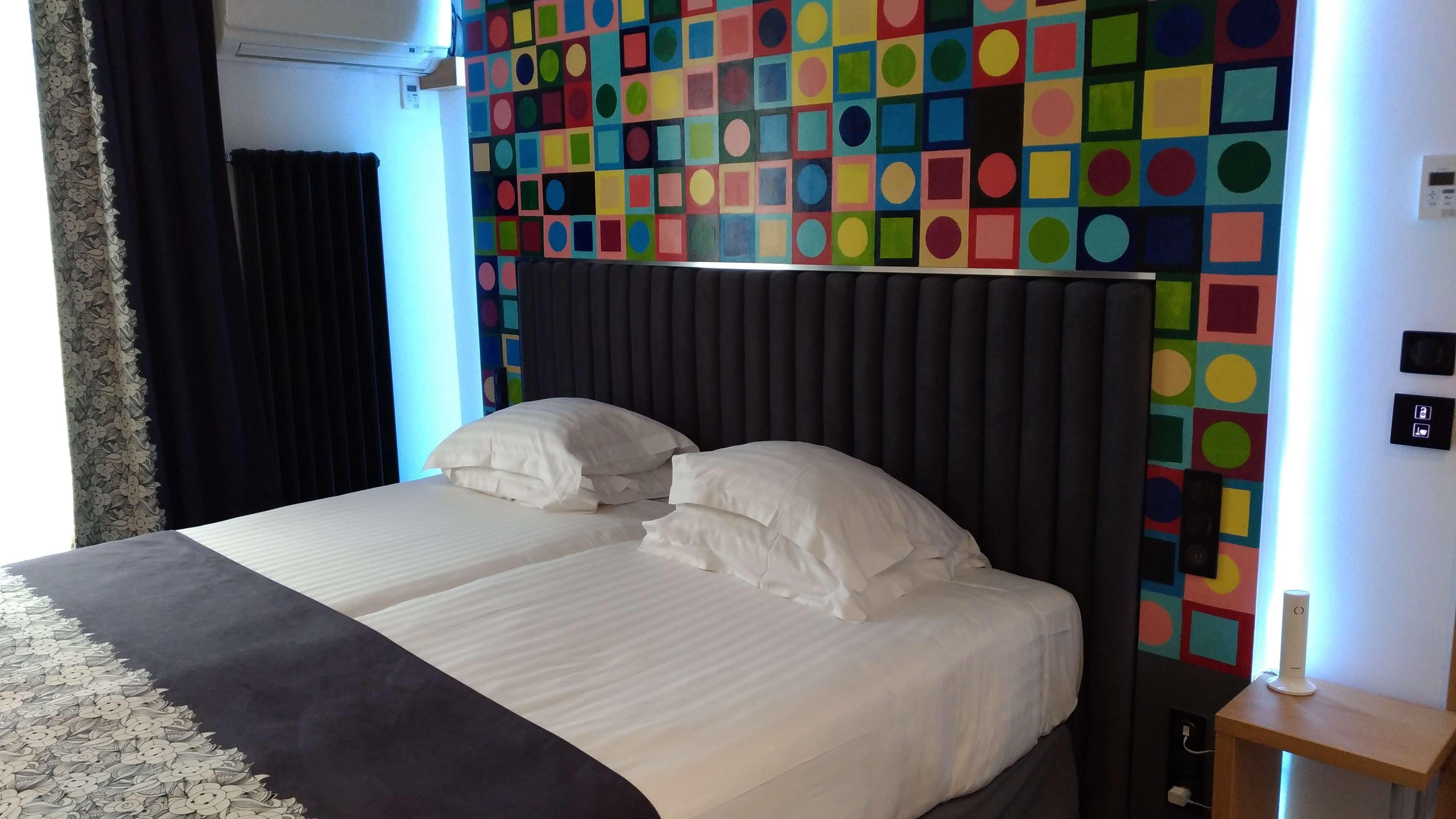 Ett hotellrum med en stor säng, en färgstark väggdekoration med geometriska mönster och ett modernt sängbord.