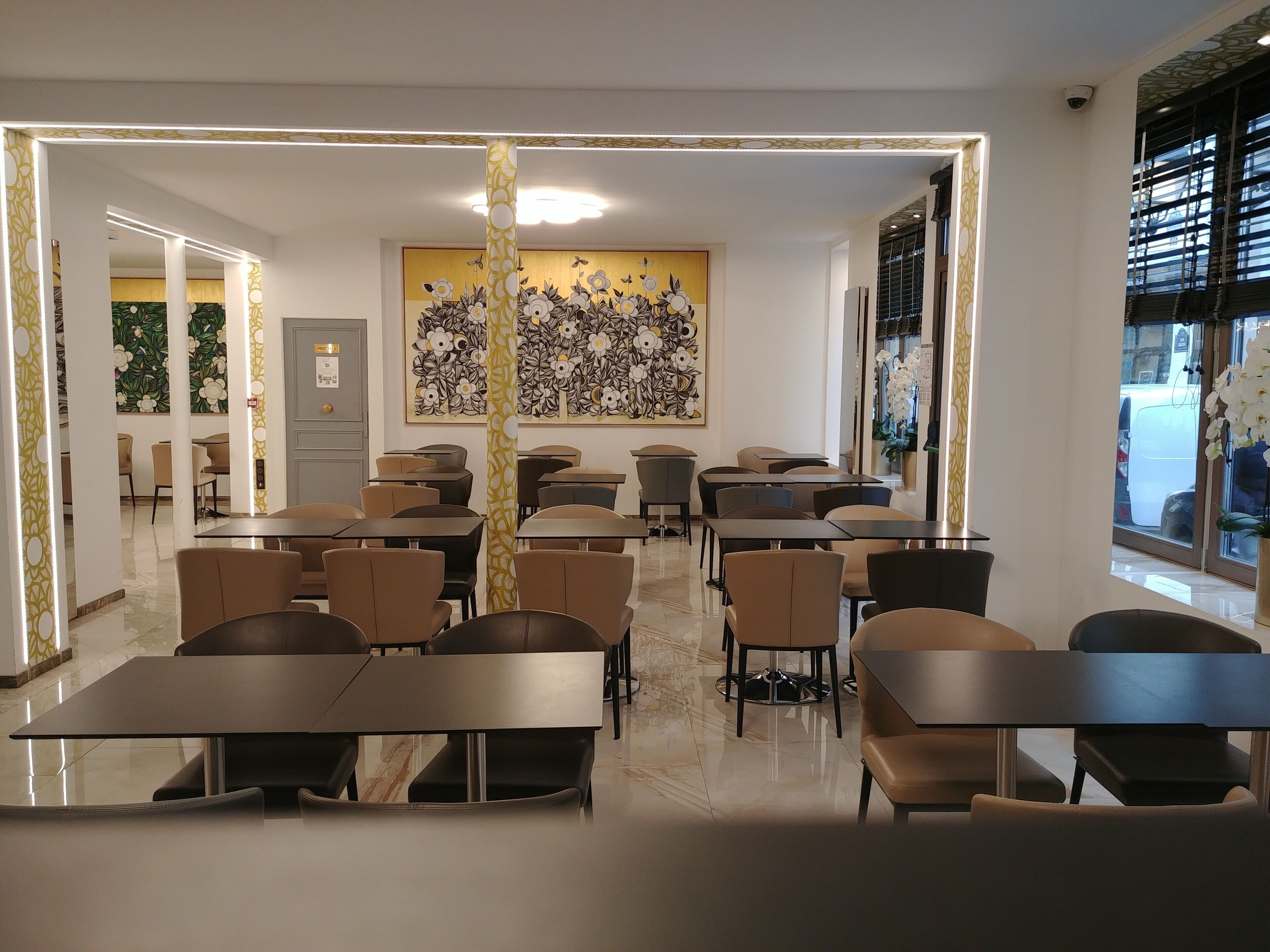 A modern dining area with tables and chairs, a decorative wall, and a view of the street outside.