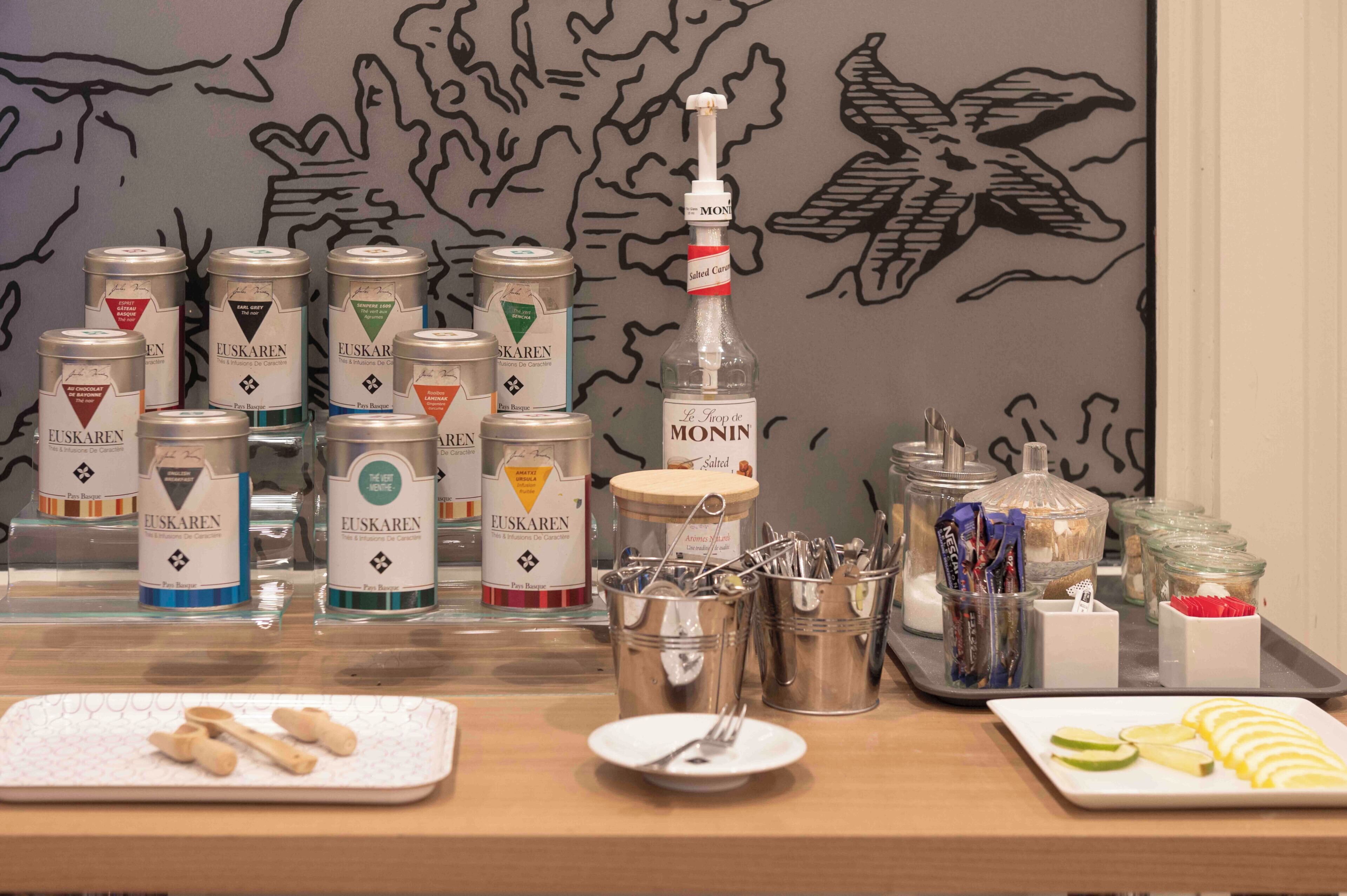 A breakfast buffet with various food items and beverages, including cans of EUSKAREN and MONIN, and a variety of utensils and condiments.
