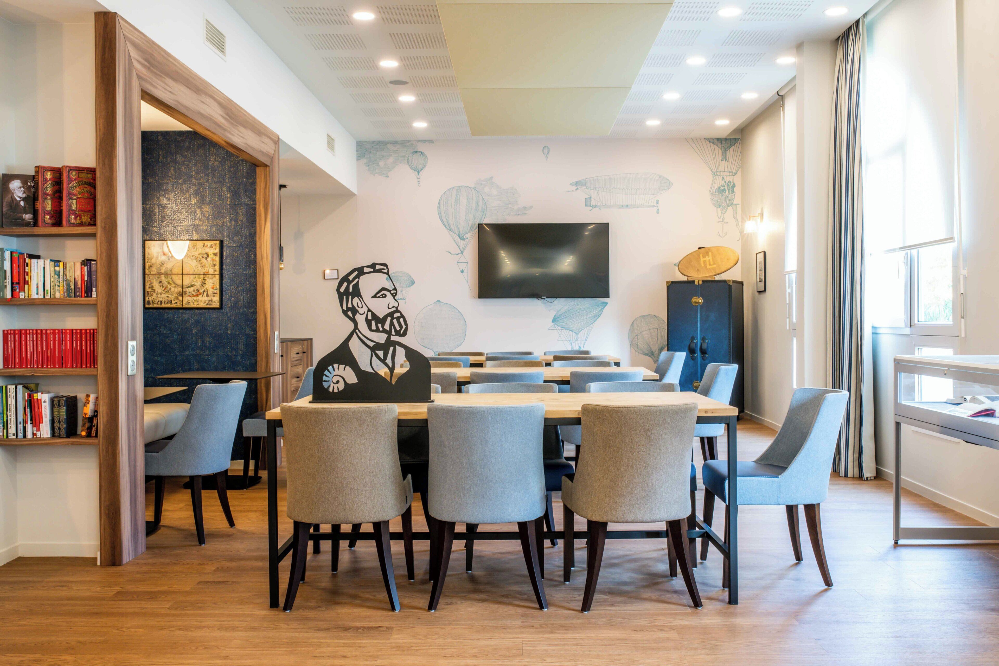 A modern conference room with a large table, chairs, a flat-screen TV, and a bookshelf with books.
