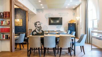 A modern conference room with a large table, chairs, a flat-screen TV, and a bookshelf with books.