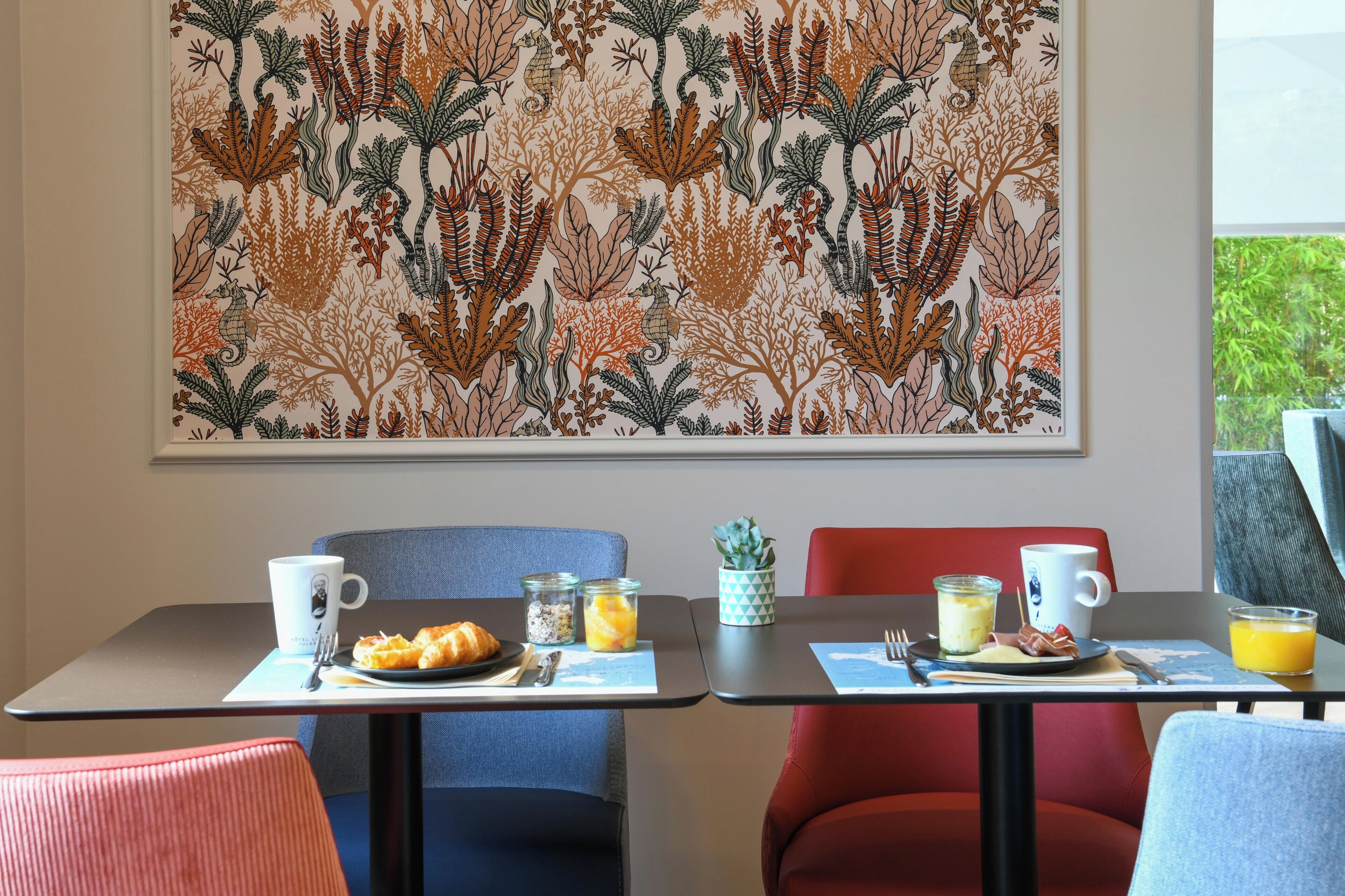 Un comedor con dos mesas, cada una con un plato de comida, una taza y un vaso de jugo. Hay sillas alrededor de las mesas y un cuadro grande en la pared.