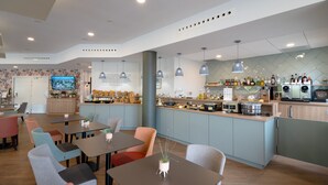 A modern restaurant with a bar area, seating with colorful chairs, and a kitchen visible in the background. - Hôtel Jules Verne Biarritz (Biarritz)