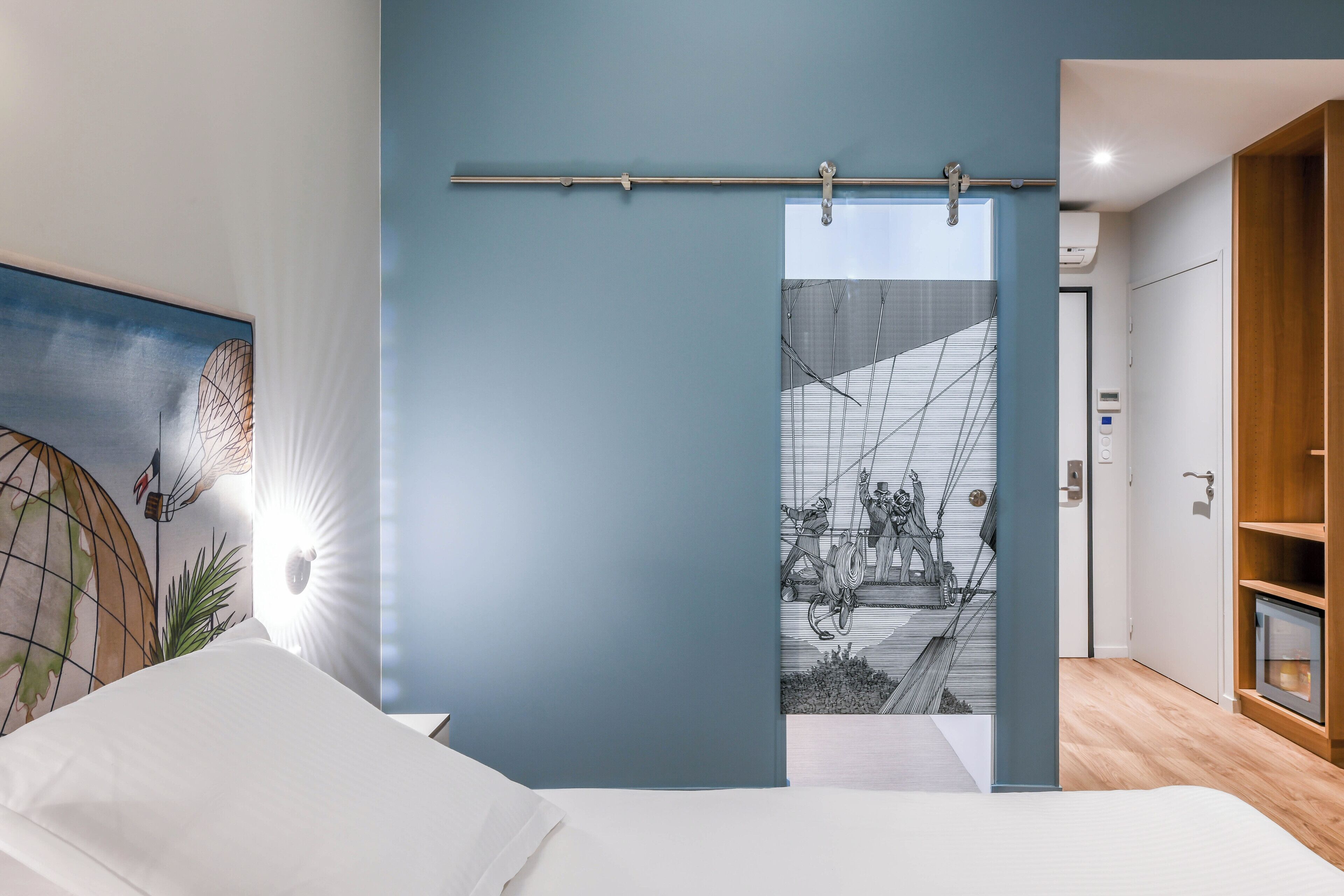Un dormitorio moderno con una cama, una lámpara de pared, un ventanal y vistas a un edificio con una escalera.