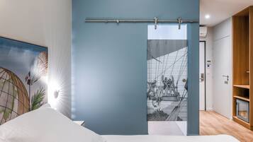 Un dormitorio moderno con una cama, una lámpara de pared, un ventanal y vistas a un edificio con una escalera.