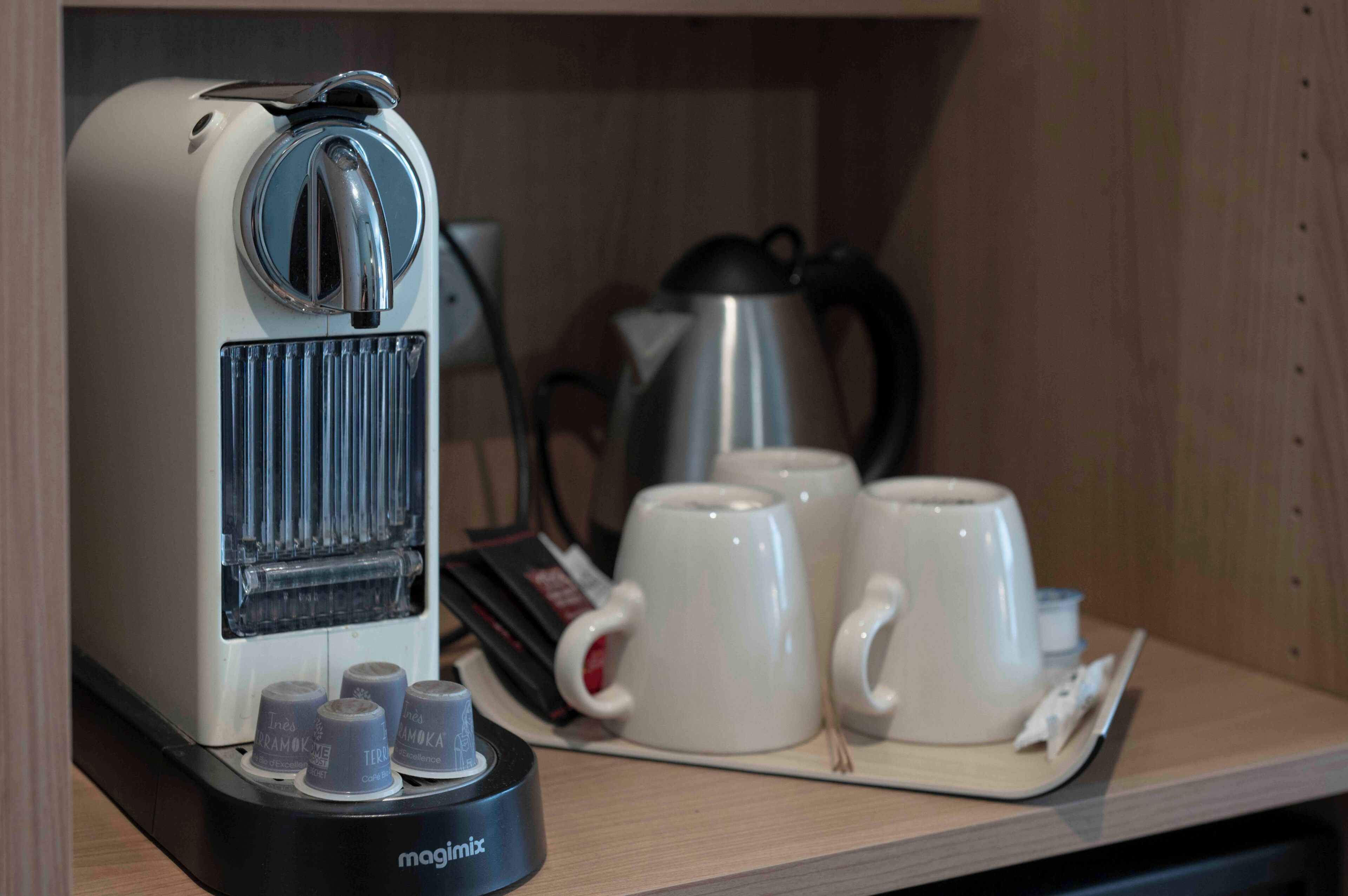 A coffee machine with a control panel and a tray with two white cups and a coffee pod.