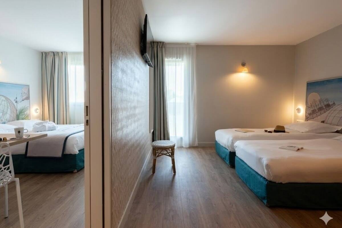 A hotel room with two beds, a desk, a chair, and a small stool.