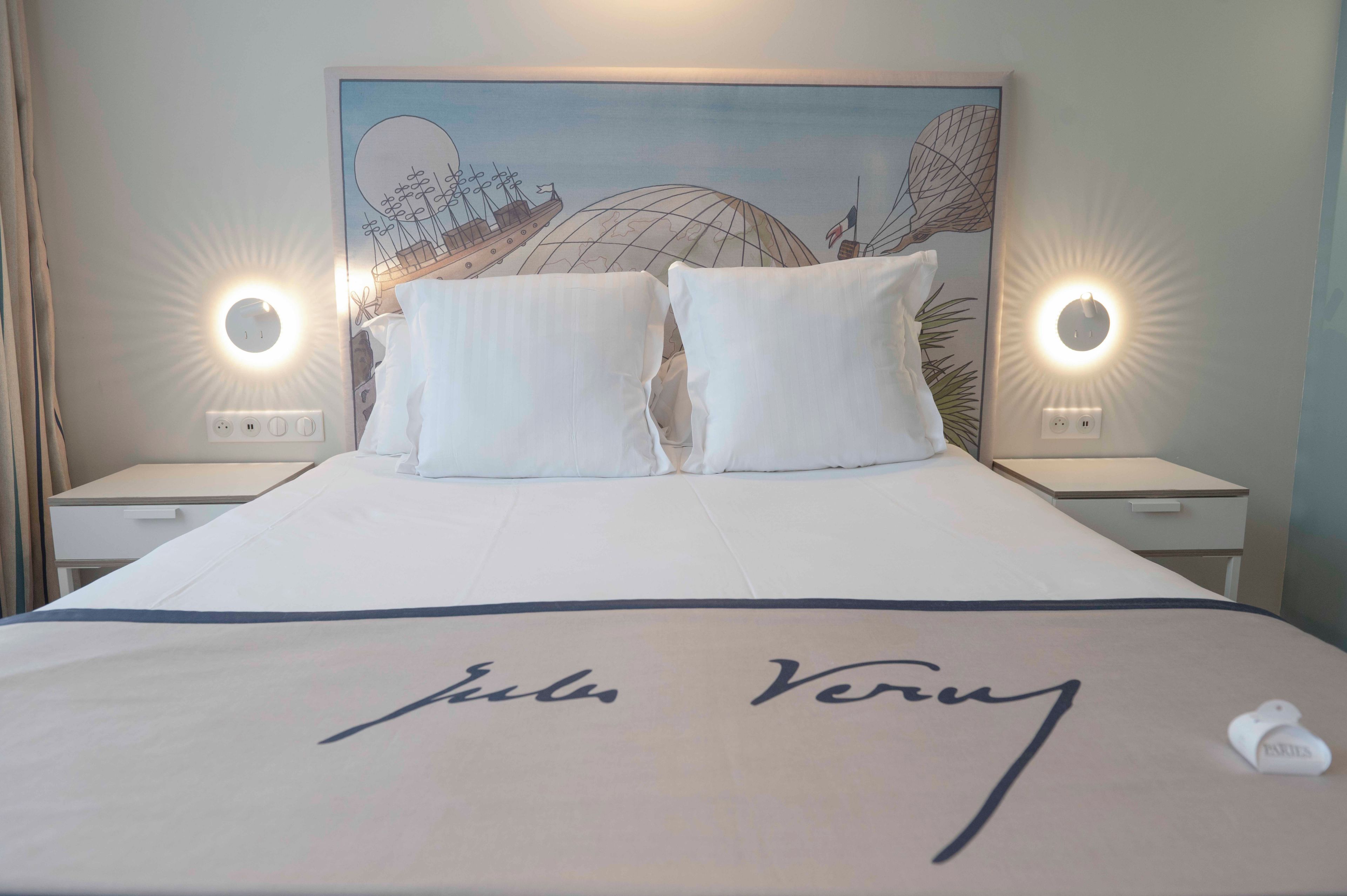 A hotel room with a large bed, two bedside tables, and a headboard with a mural.
