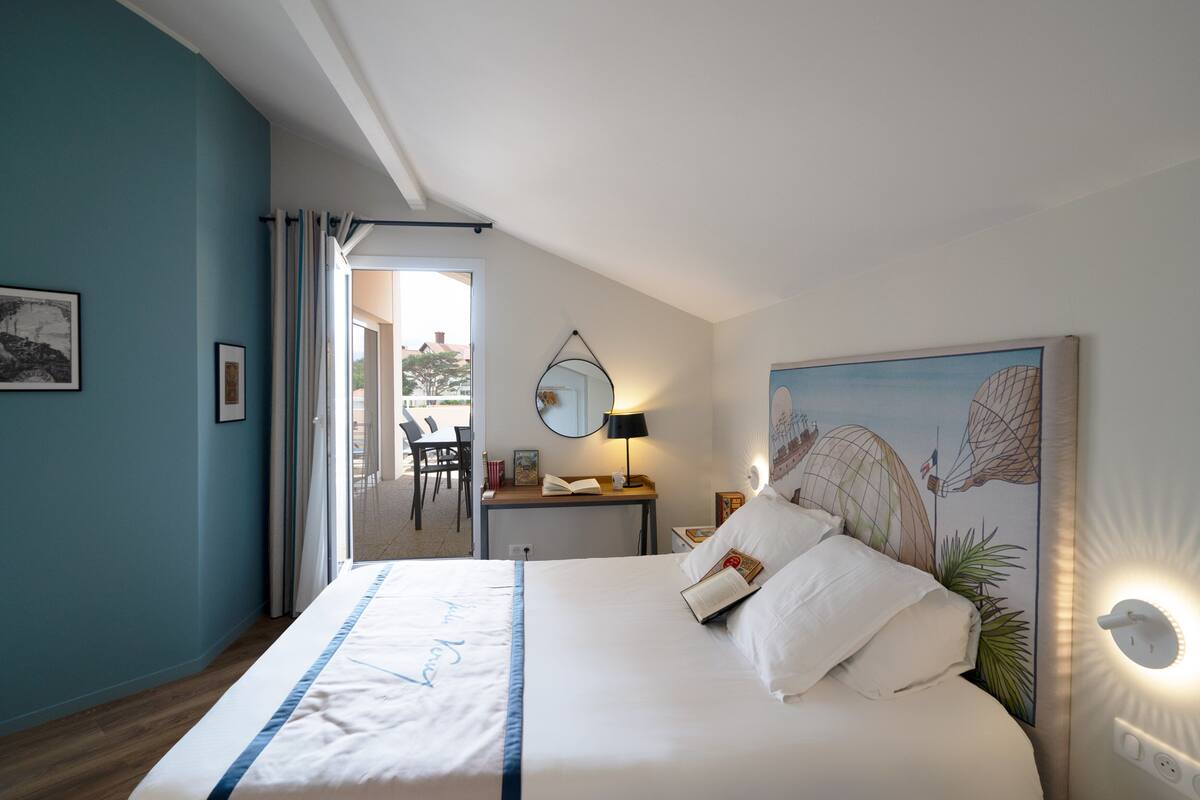 A bedroom with a bed, a desk, a chair, a window, and a painting on the wall.