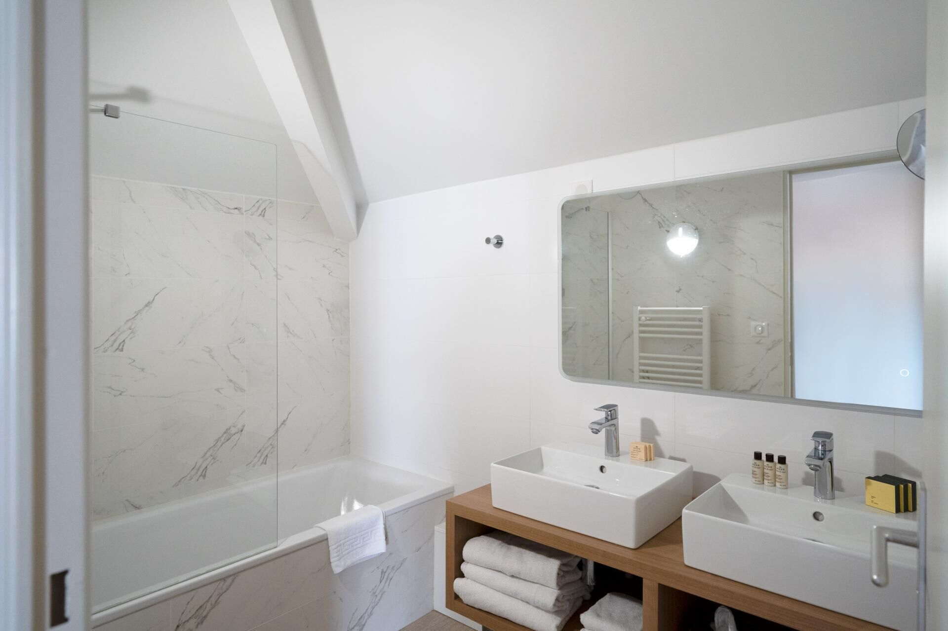 A modern bathroom with a bathtub, two sinks, a large mirror, and a towel rack.