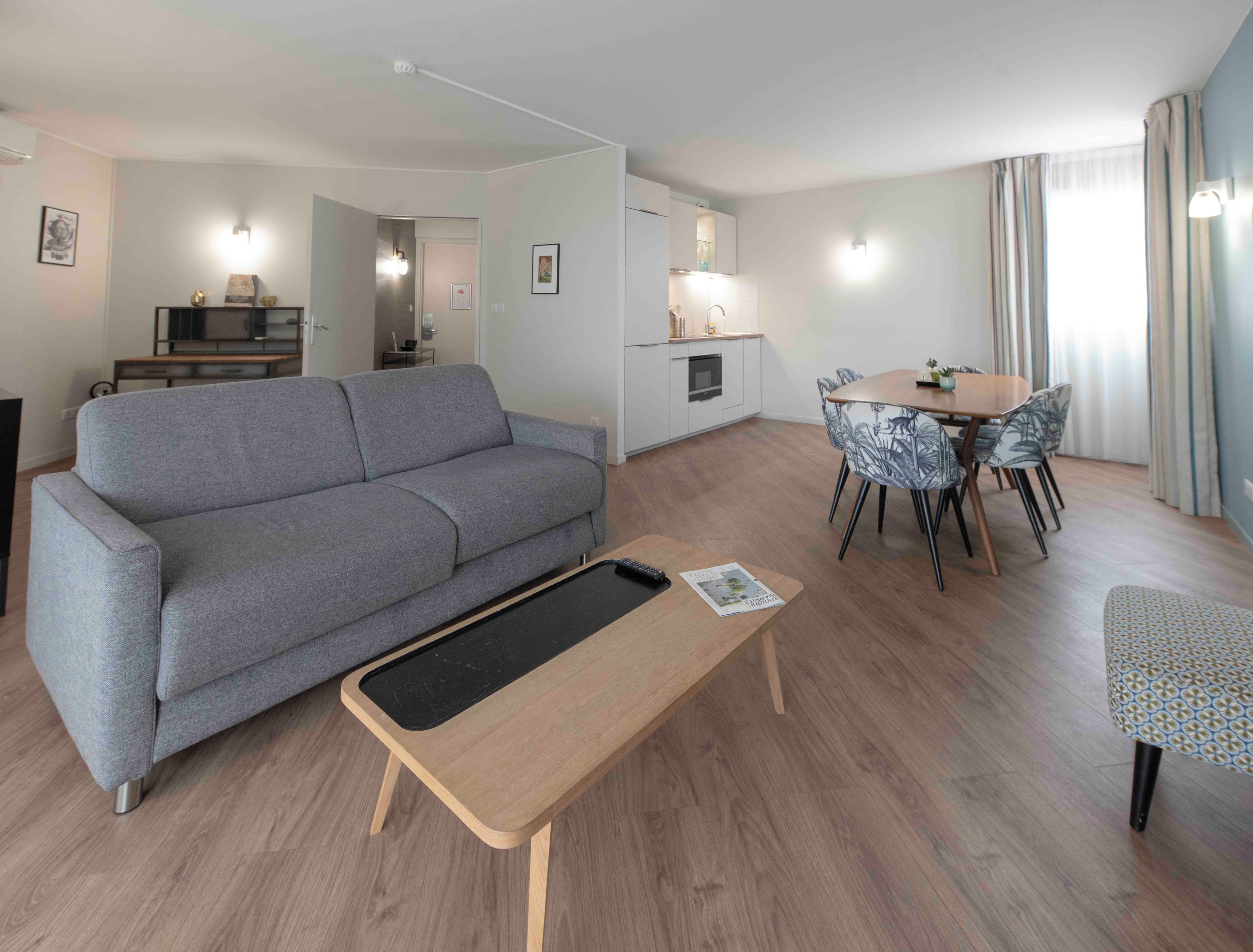 Un salon moderne avec un canapé gris, une table basse en bois et un coin repas doté de chaises à motifs.
