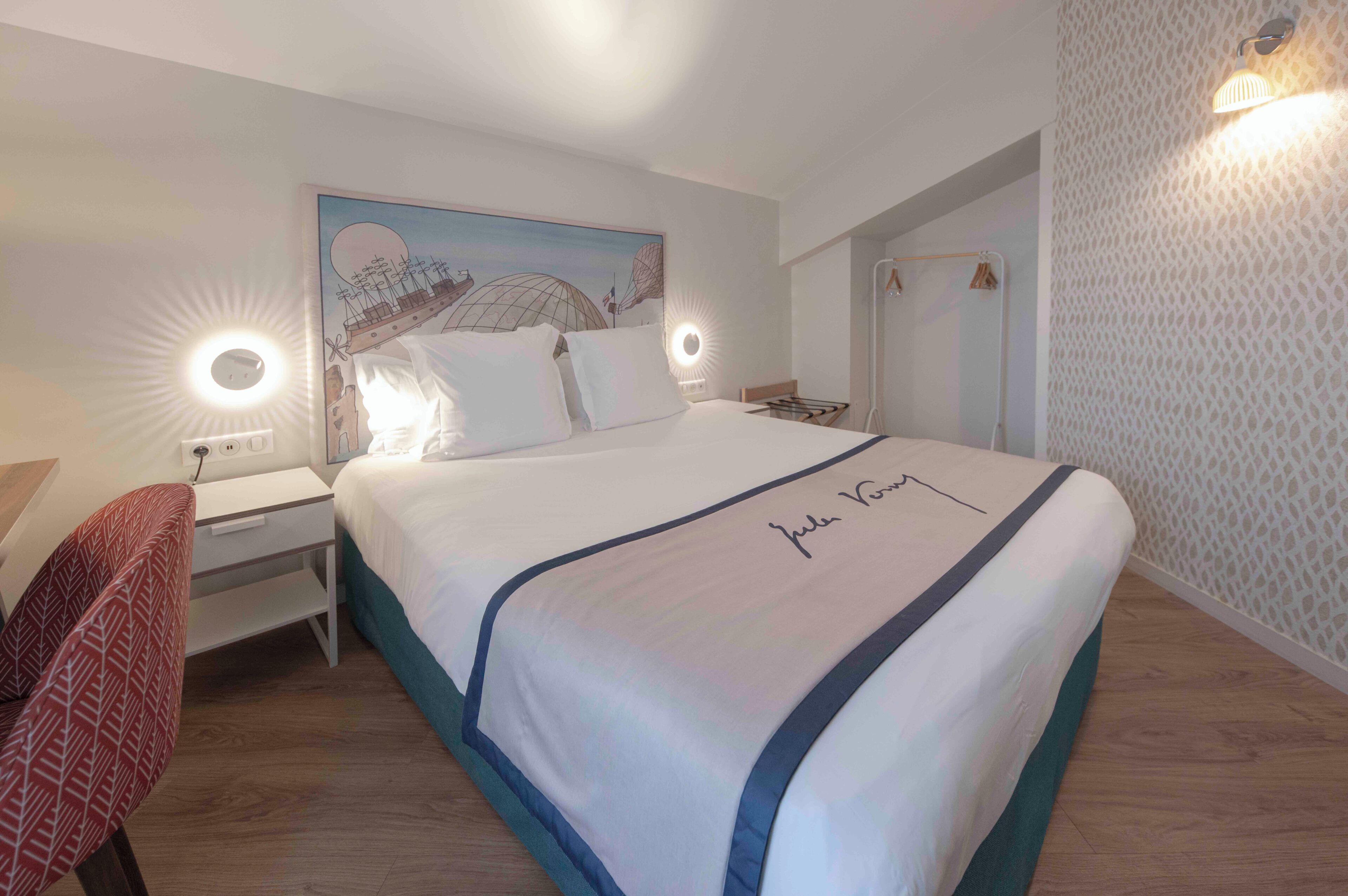 A hotel room with a bed, bedside table, lamp, and a wall with a patterned design.