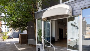 Una entrada de hotel moderna con fachada de vidrio, un toldo curvo y una escalera que conduce a la entrada.