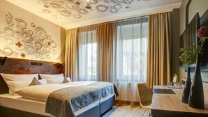 Una habitación de hotel moderna con una cama grande, un escritorio y un techo decorativo.