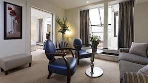A modern hotel room with a sofa, two armchairs, a small round table, and a large window with curtains. - Le Pera (Paris)