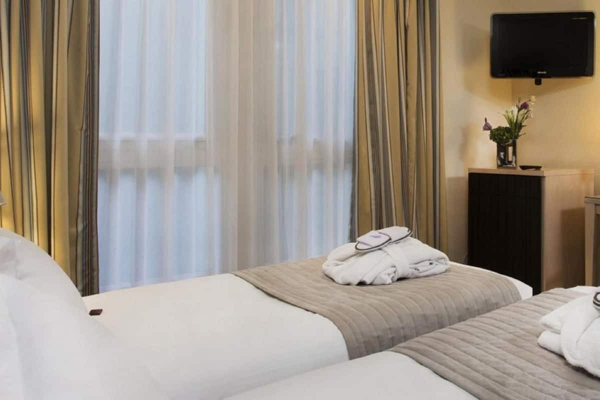 Une chambre d’hôtel avec deux lits, un bureau, une chaise, une télévision et un miroir.
